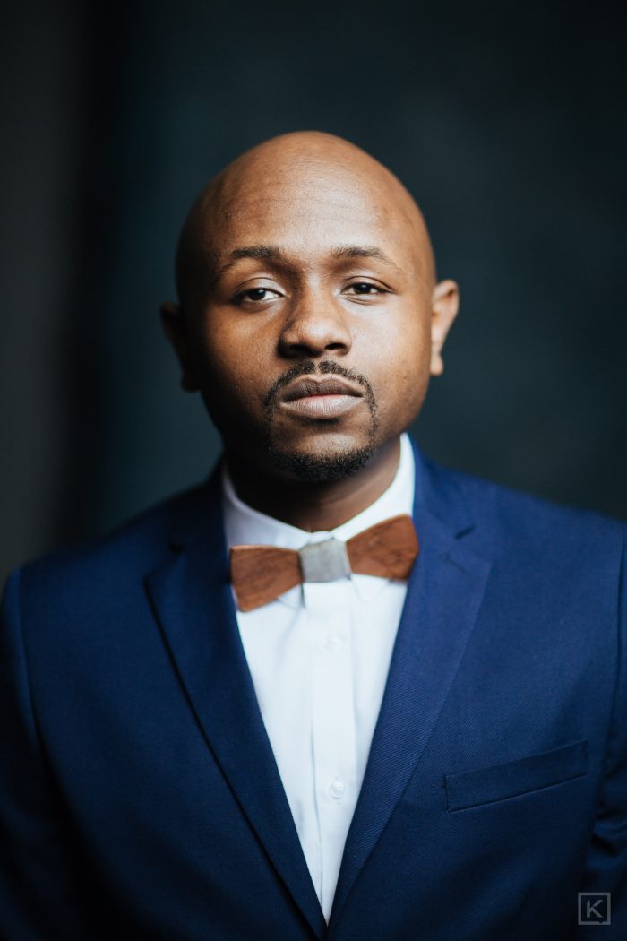 Ryan Perez in a navy suit and wooden bow tie, steady direct gaze
